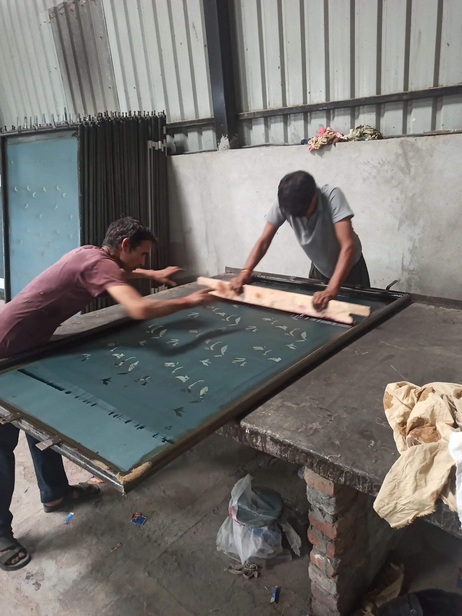 Artisans manually pulling squeegee over screen printing table